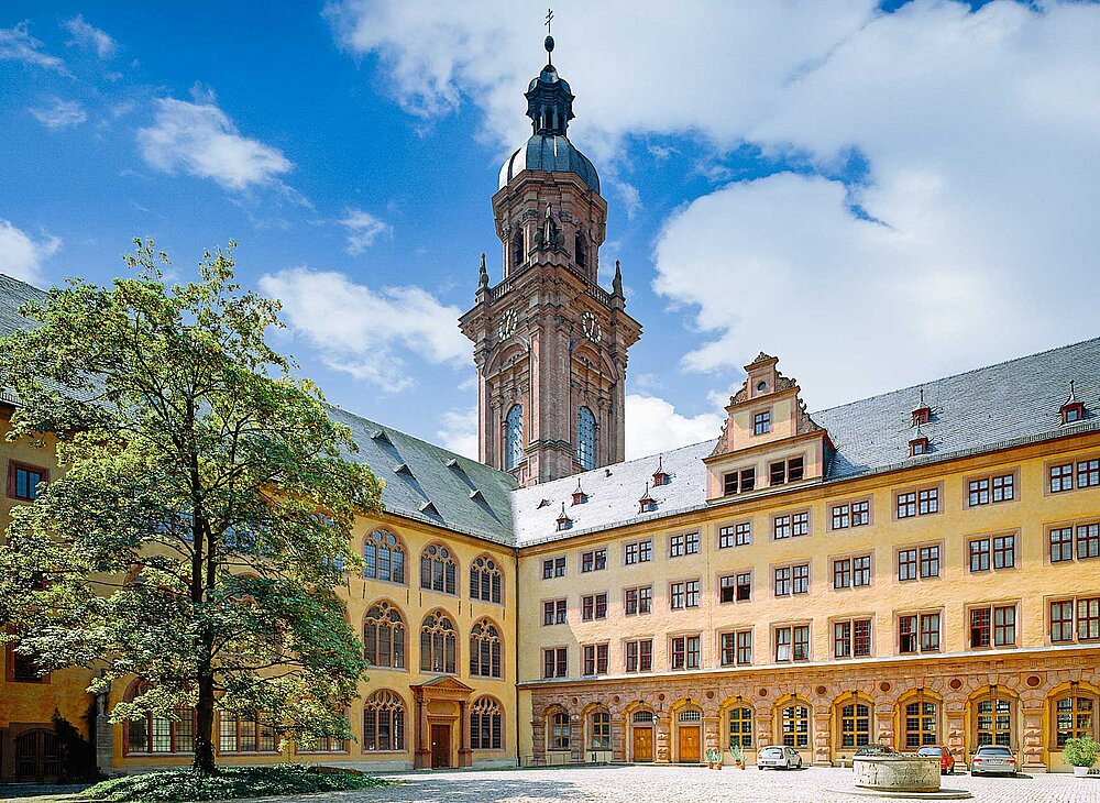 Das Foto zeigt den rötlichen Turm der Neubaukirche und die Räumlichkeiten der Juristischen Fakultät, aufgenommen aus dem Innenhof der Juristischen Fakultät.