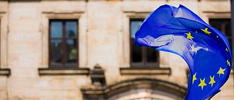 Die Flagge der Europäischen Union weht im Wind vor einem steinernen Gebäude.
