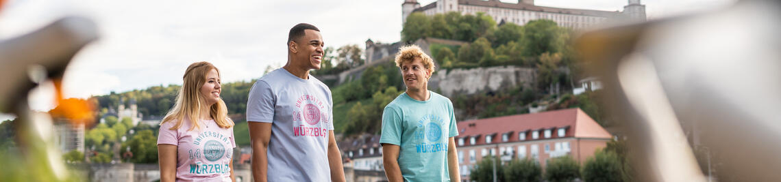 Drei Studierende tragen T-Shirts mit einem Aufdruck der Universität Würzburg.